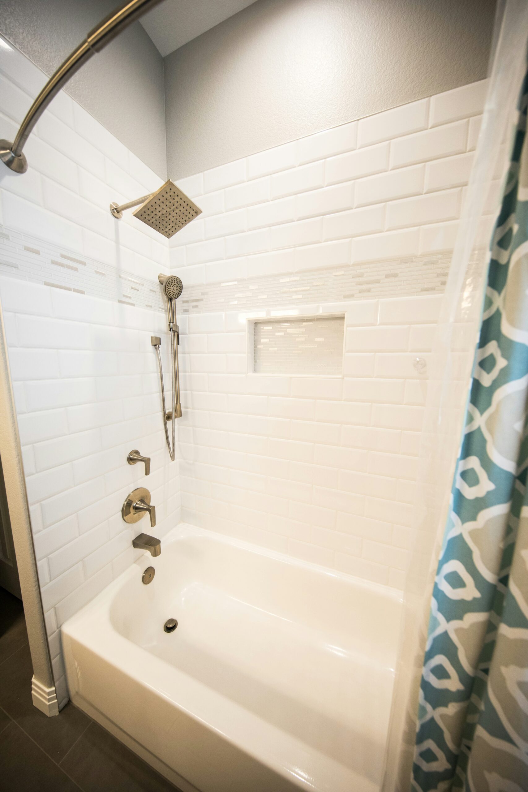 Custom shower and bathtub in white subway tile with chrome finishes and a blue and white shower curtain